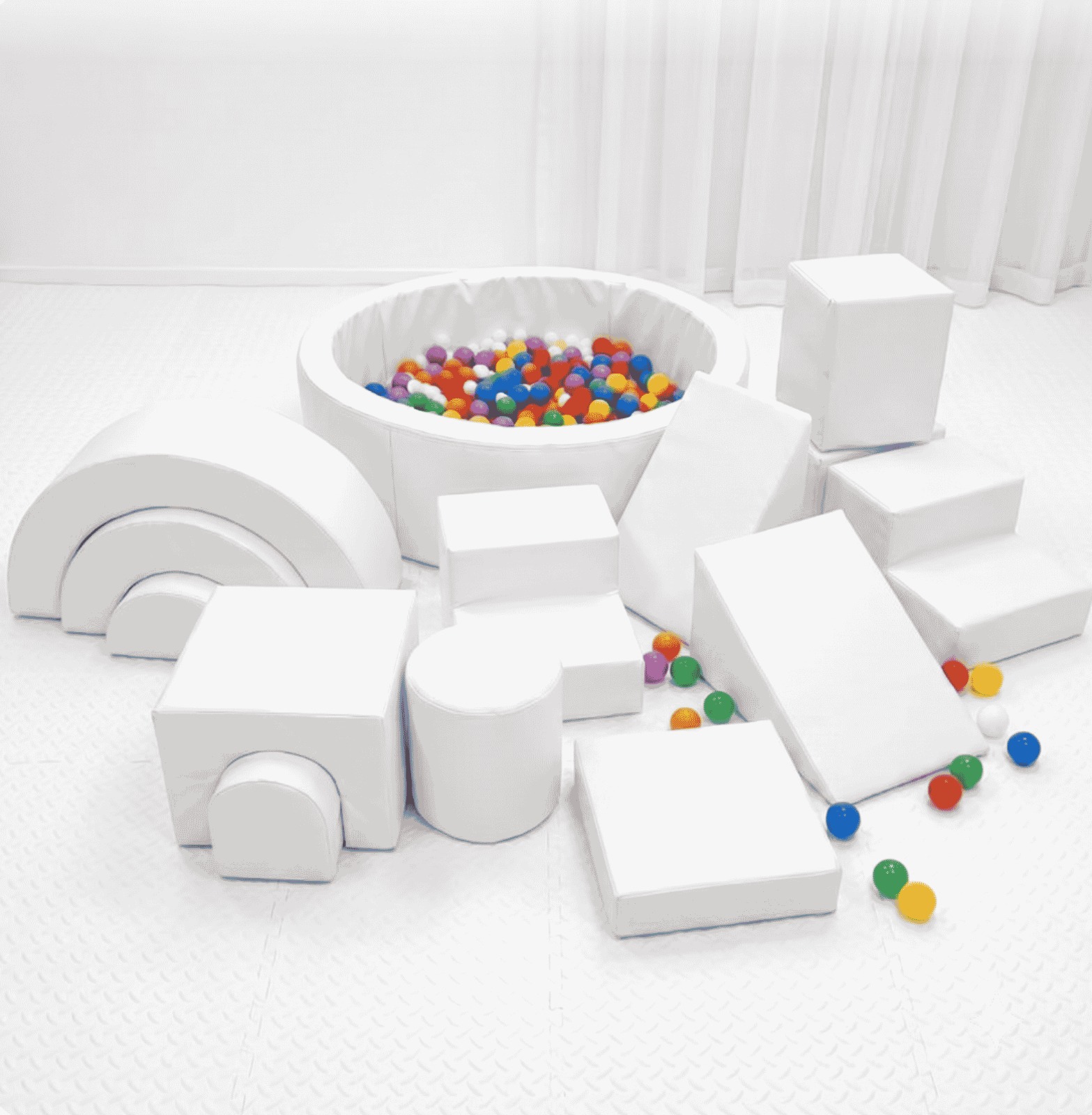 A luxury all-white soft play setup featuring a chic ball pit, white foam climbing blocks, and a mini slide on a clean white play mat